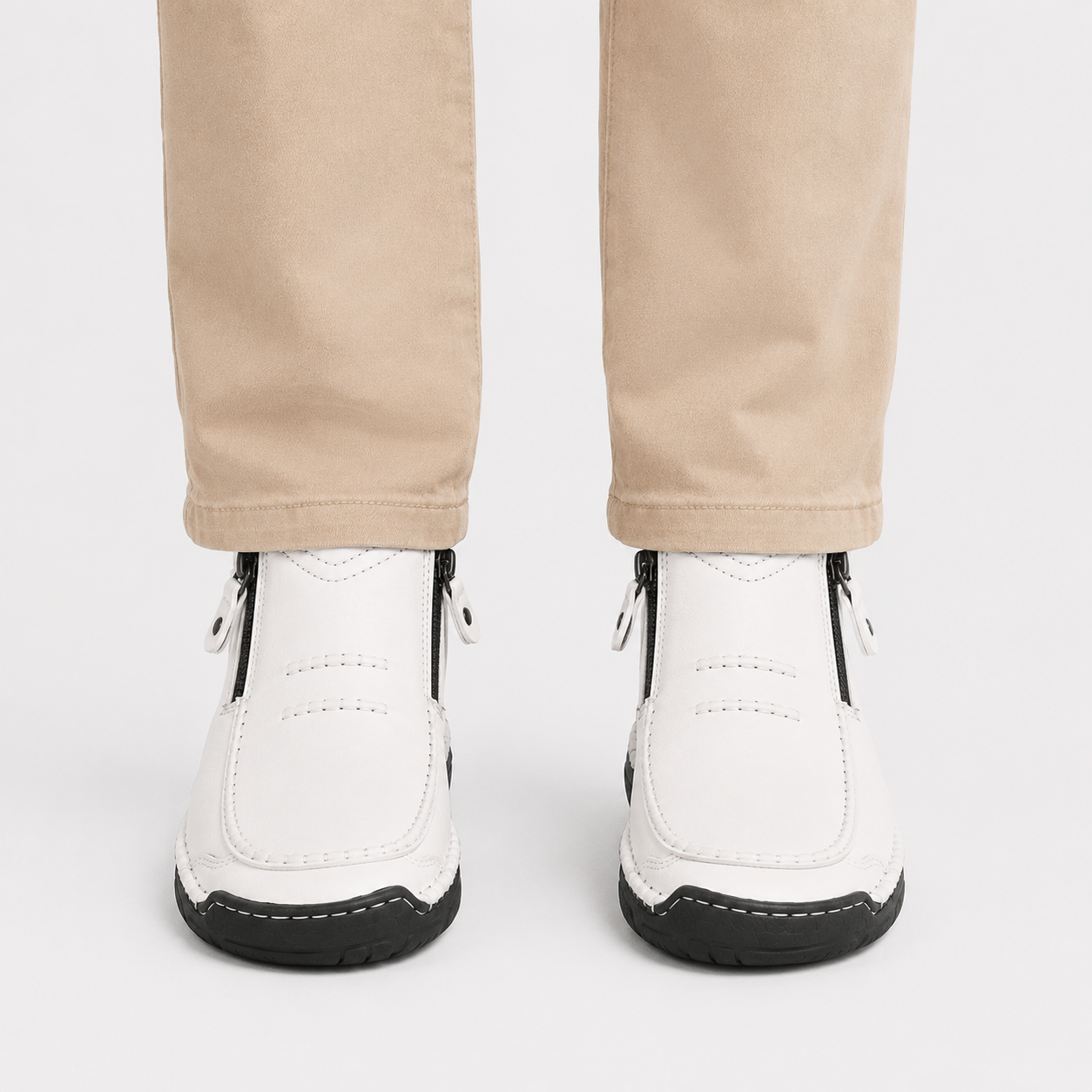 White ankle boots with black soles and side zippers, shown on a model wearing beige trousers against a light gray background.