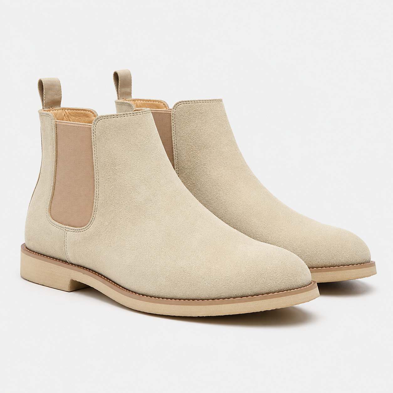 A pair of beige suede Chelsea boots with elastic side panels and pull tabs, shown on a clean light gray background.