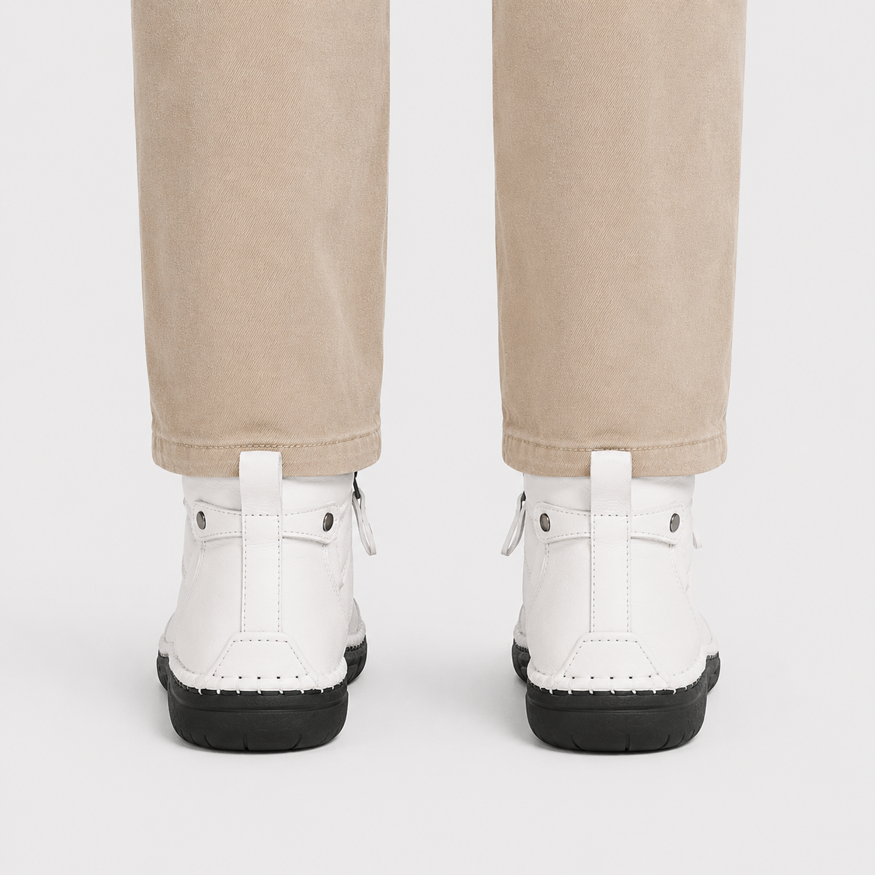 White ankle boots with black soles and pull tabs, shown from the back on a model wearing beige pants against a light gray background.