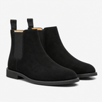 A pair of black suede Chelsea boots with black elastic side panels and pull tabs, shown on a clean white background.