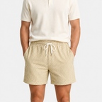 A model wearing beige and white vertically striped drawstring shorts with a cream polo shirt, shown from the chest down against a light gray background.