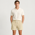 A man modeling a short-sleeve polo shirt and striped drawstring shorts against a light gray studio background.