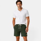 Man wearing a white polo shirt and green shorts on a plain background