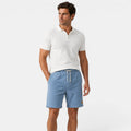Man wearing a white polo shirt and blue shorts on a white background