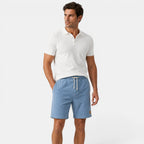 Man wearing a white polo shirt and blue shorts on a white background