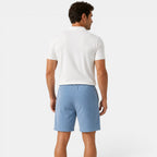 Man wearing a white polo shirt and light blue shorts on a white background