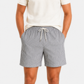 A person wearing gray and white vertically striped drawstring shorts with a cream t-shirt, shown from the chest down against a light gray studio background.