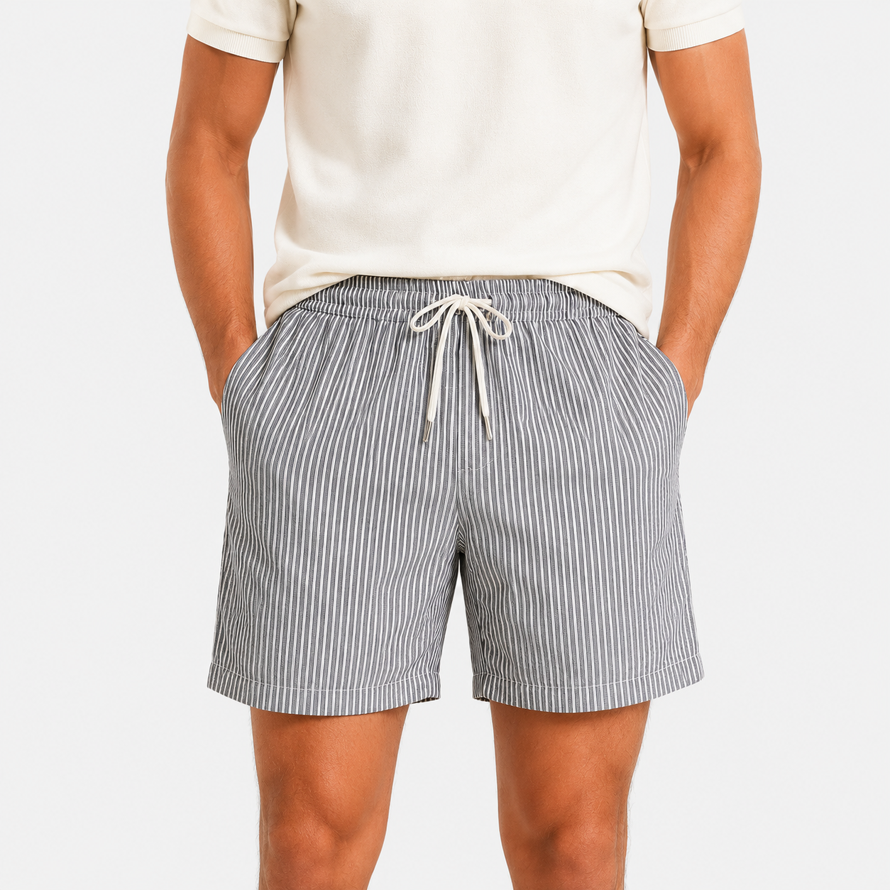 A person wearing gray and white vertically striped drawstring shorts with a cream t-shirt, shown from the chest down against a light gray studio background.