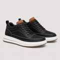 A pair of black low-top lace-up sneakers with a chunky white platform sole, brown collar lining, and black laces, photographed on a light gray studio background.