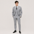 A man modeling a light gray three-piece suit with a matching vest, white dress shirt, black tie, and black dress shoes against a plain light gray studio background.