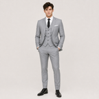 A man modeling a light gray three-piece suit with a matching vest, white dress shirt, black tie, and black dress shoes against a plain light gray studio background.