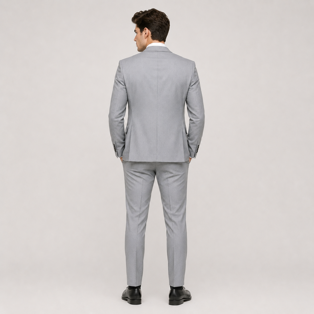 A man wearing a light gray two-piece suit, shown from the back, standing against a neutral light gray studio background.