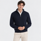 A man wearing a navy blue cable-knit quarter-zip sweater over a white collared shirt and beige trousers, standing against a plain white studio background.