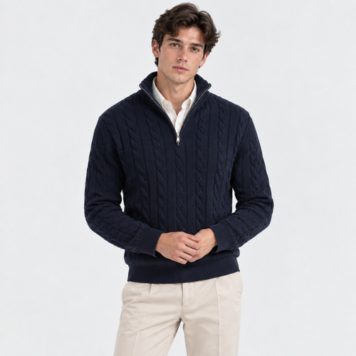 A man wearing a navy blue cable-knit quarter-zip sweater over a white collared shirt and beige trousers, standing against a plain white studio background.