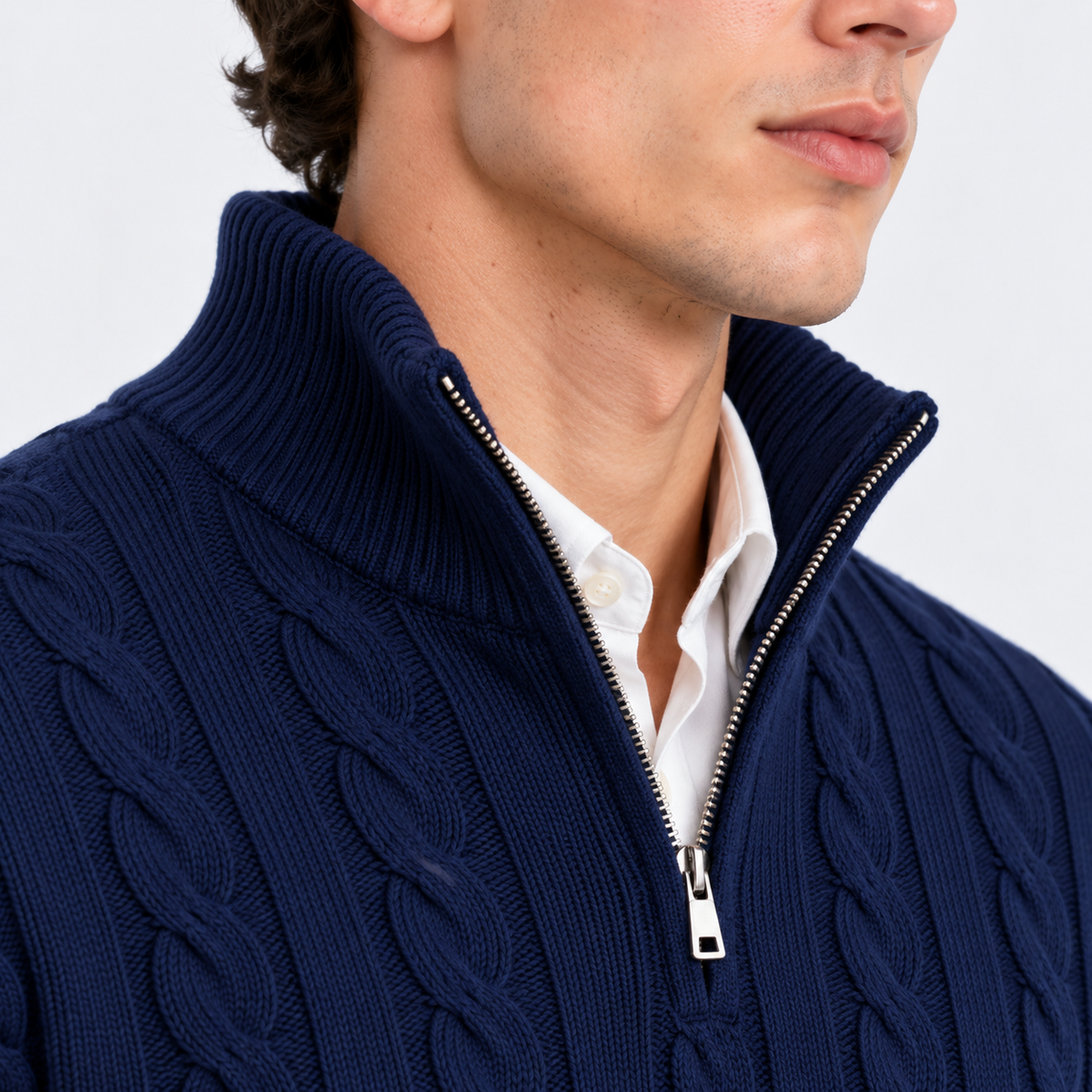 Close-up of a man wearing a navy blue cable-knit zip-up sweater over a white collared shirt, against a light gray background.
