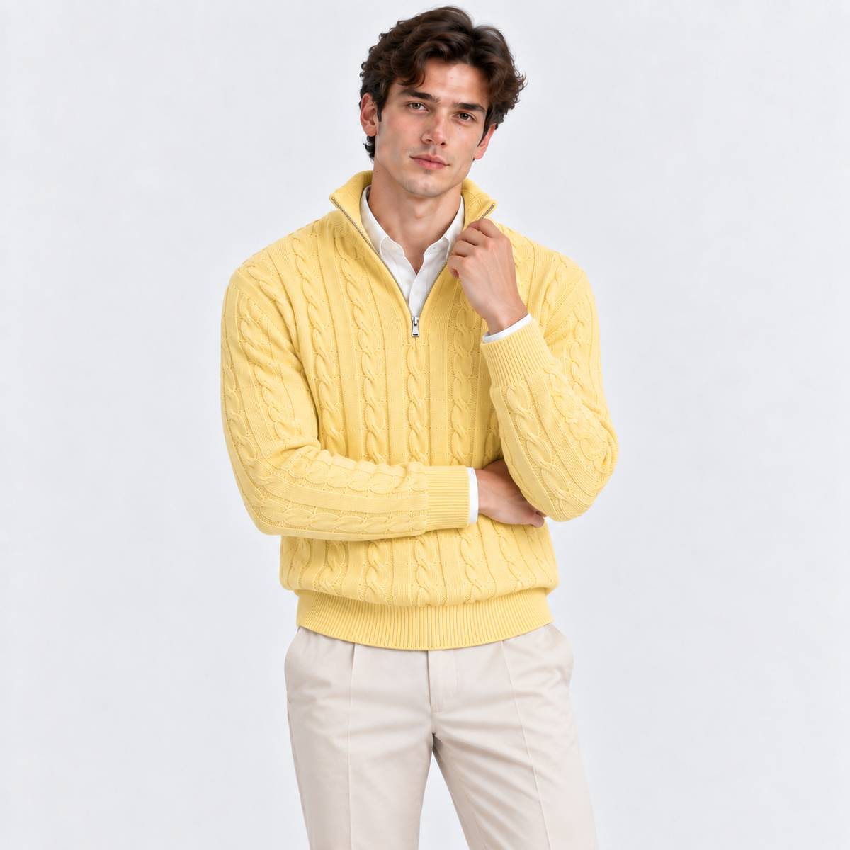 A man wearing a yellow cable-knit quarter-zip sweater over a white collared shirt and beige trousers, standing against a light gray studio background.