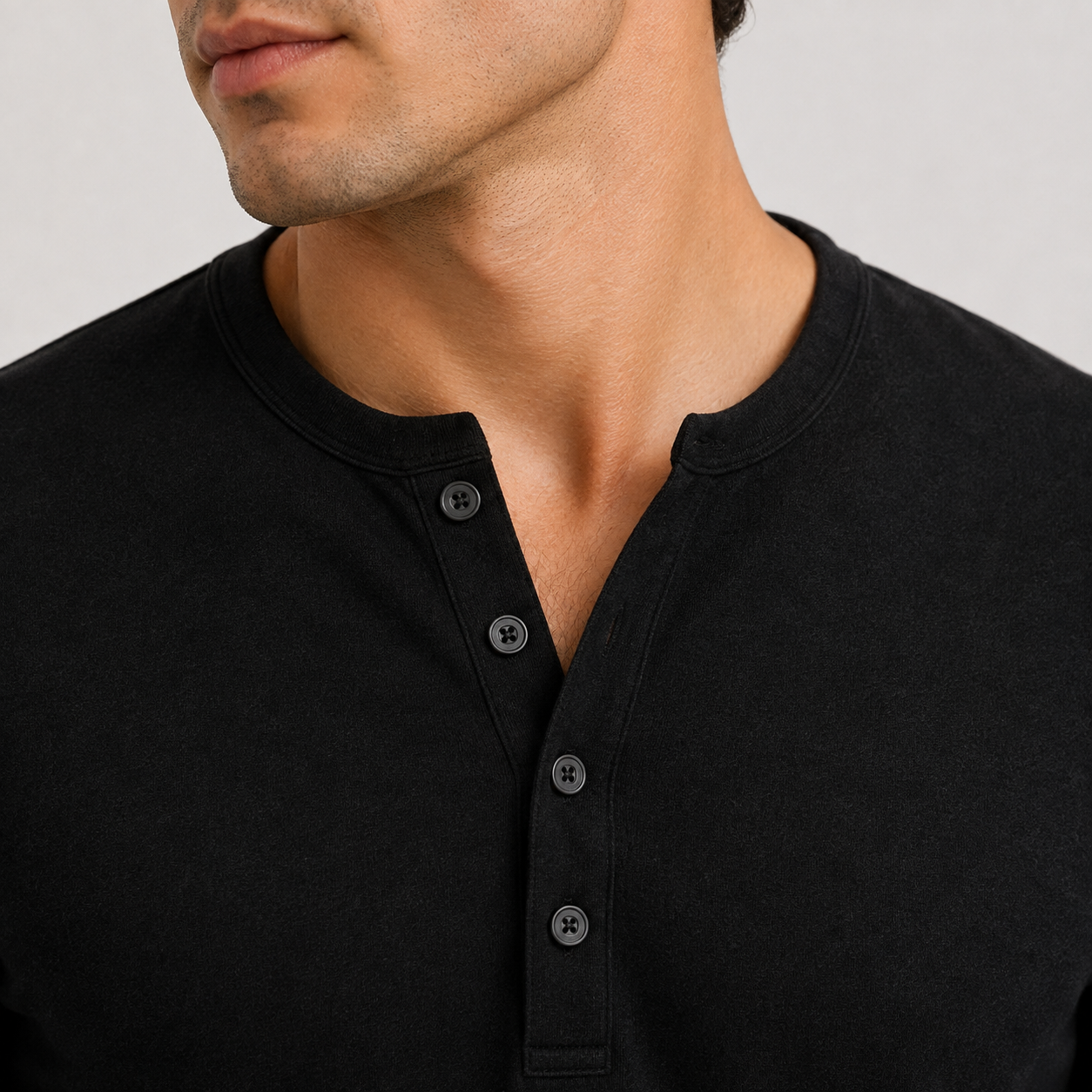Close-up of a man wearing a black Henley shirt with a three-button placket, showing the fabric texture and neckline details.