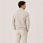 A man shown from the back wearing a light beige knit sweater and matching trousers against a plain light background.