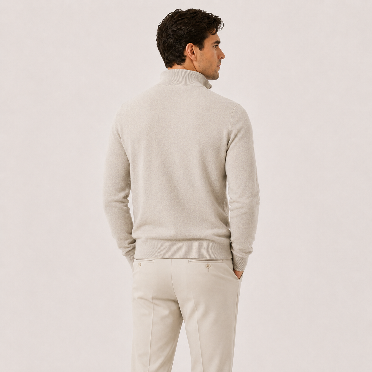 A man shown from the back wearing a light beige knit sweater and matching trousers against a plain light background.