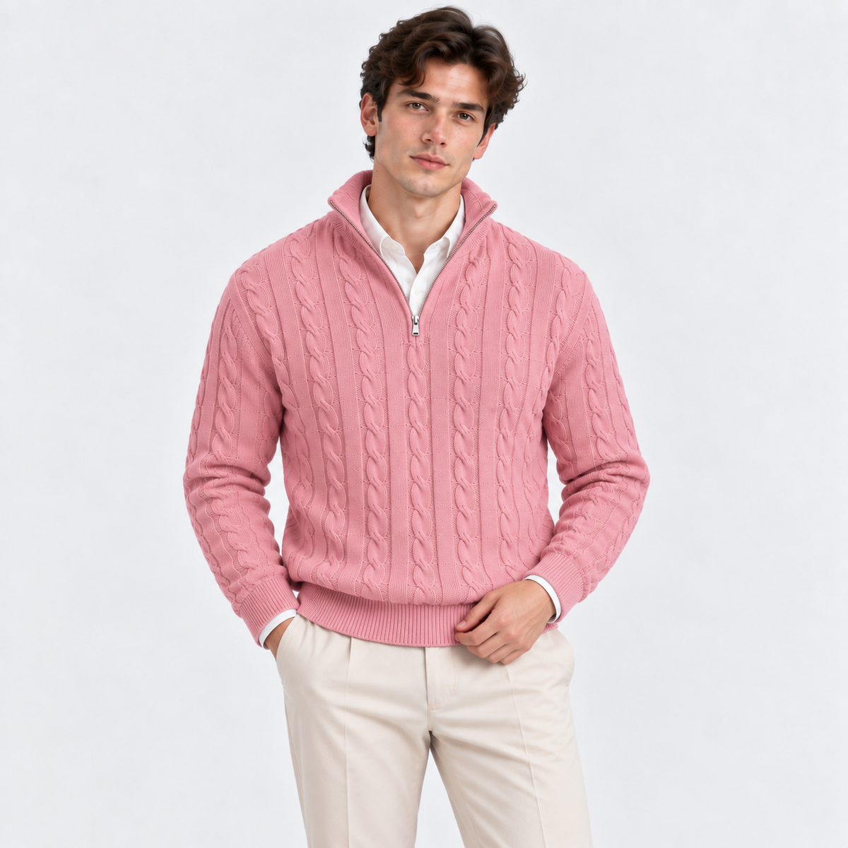 A man wearing a pink cable-knit quarter-zip sweater over a white collared shirt and cream trousers, standing against a plain light gray studio background.
