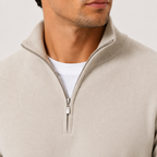 Close-up of a man wearing a light beige quarter-zip sweater over a white t-shirt, showing the ribbed collar and silver zipper.