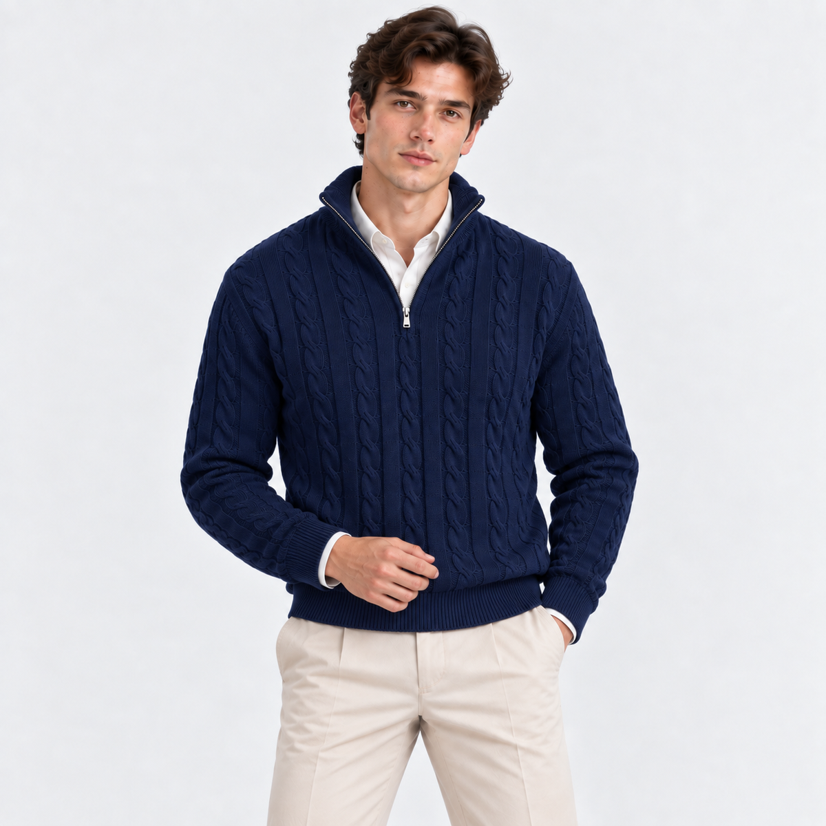 A man wearing a navy blue cable-knit quarter-zip sweater over a white collared shirt and beige trousers, standing against a light gray studio background.