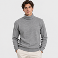 A man wearing a light gray ribbed turtleneck sweater and cream pants, standing against a light gray studio background.