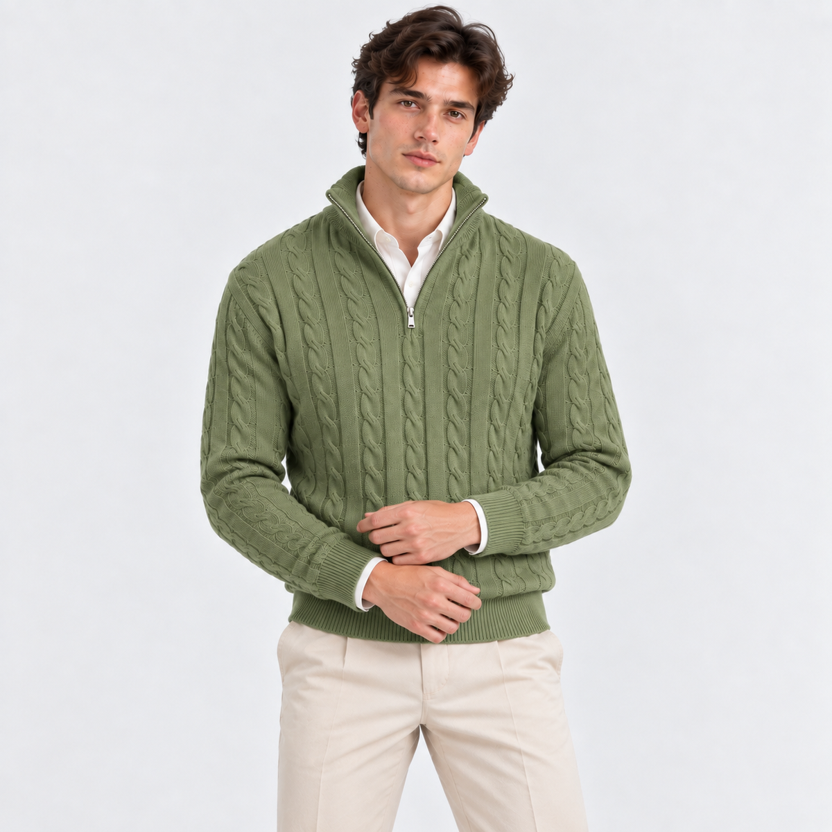 A man wearing an olive green cable-knit quarter-zip sweater over a white collared shirt and beige trousers, standing against a light gray studio background.