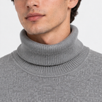 Close-up of a man wearing a gray ribbed turtleneck sweater against a light gray background.
