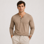 A man wearing a light brown long-sleeve henley shirt and beige trousers, standing against a light gray studio background.