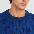 Close-up of a man wearing a textured royal blue knit sweater with a cable pattern on the chest, showing the crew neck and upper torso against a light gray background.