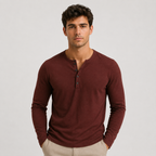 A man wearing a long-sleeve henley shirt in a deep burgundy color, paired with light beige pants, standing against a plain light gray studio background.