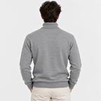 A man viewed from behind wearing a light gray ribbed mock neck sweater and cream pants, set against a plain light gray studio background.