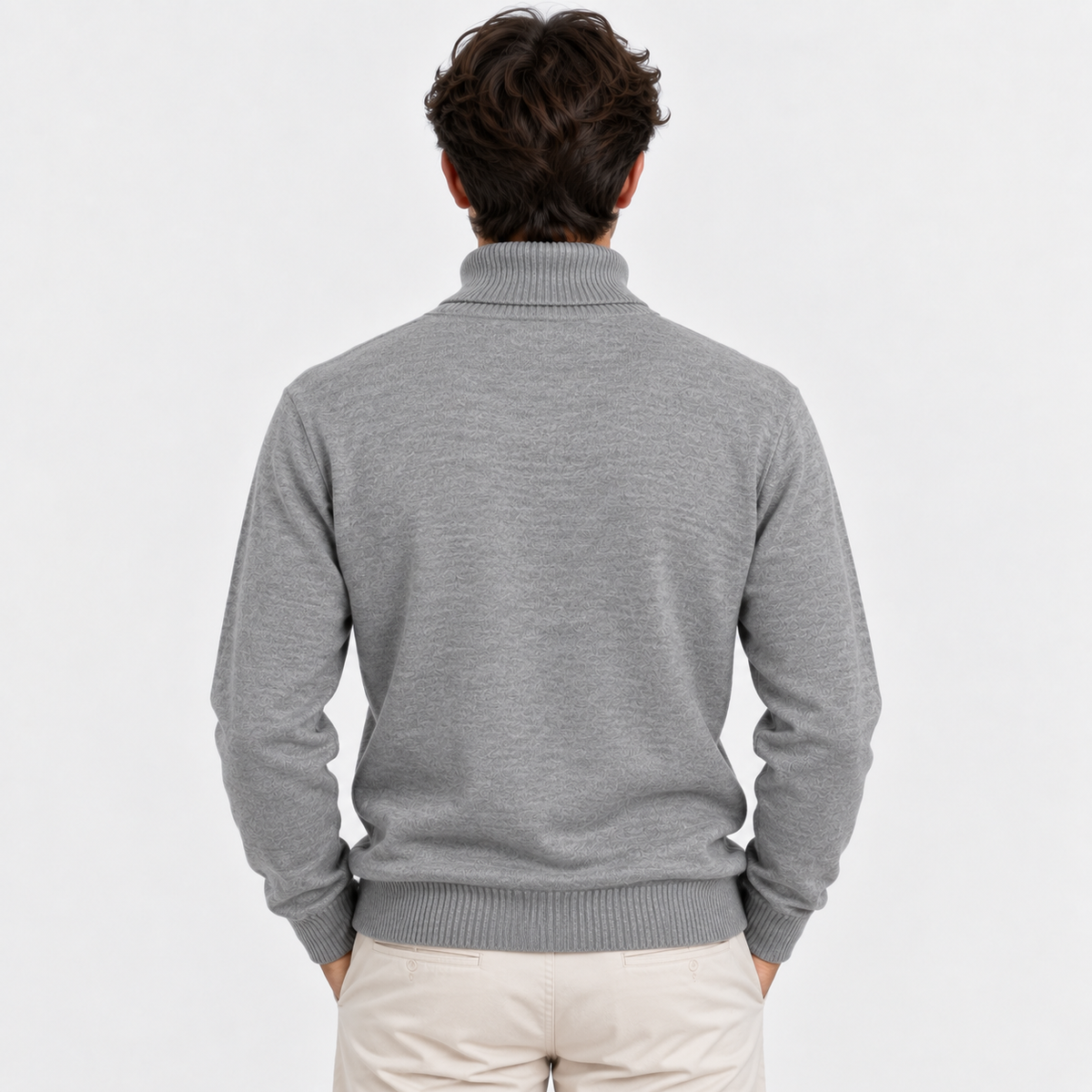 A man viewed from behind wearing a light gray ribbed mock neck sweater and cream pants, set against a plain light gray studio background.