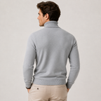 A man wearing a light gray ribbed turtleneck sweater, shown from the back, paired with beige trousers, against a plain light gray studio background.