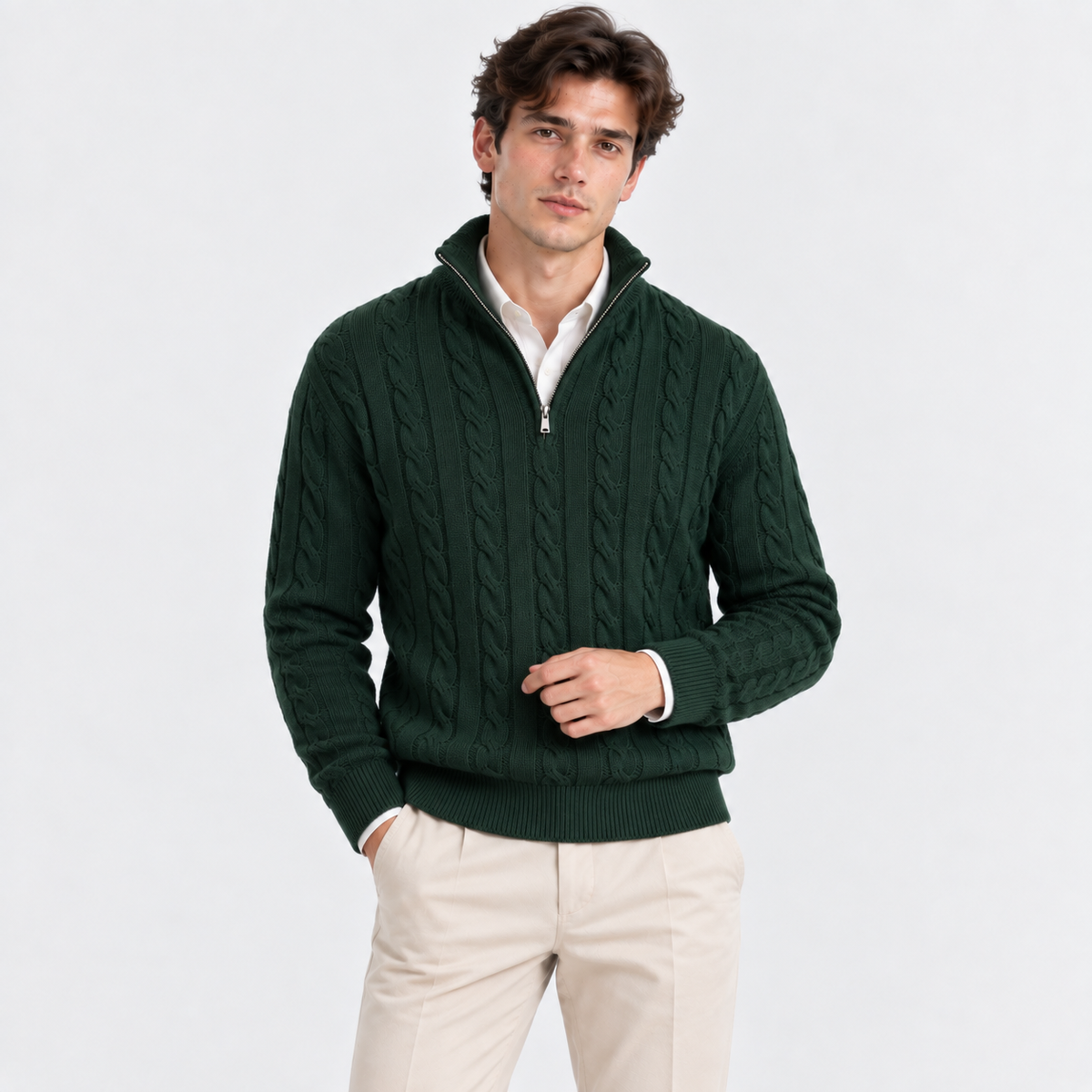 A man wearing a dark green cable-knit quarter-zip sweater over a white collared shirt and beige trousers, standing against a light gray studio background.