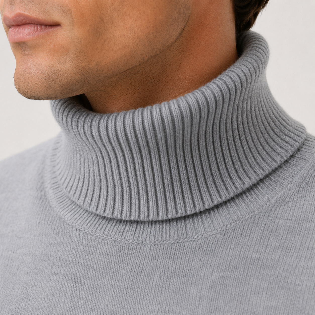 Close-up of a man wearing a light gray ribbed turtleneck sweater, showing the collar texture and part of his lower face and neck.