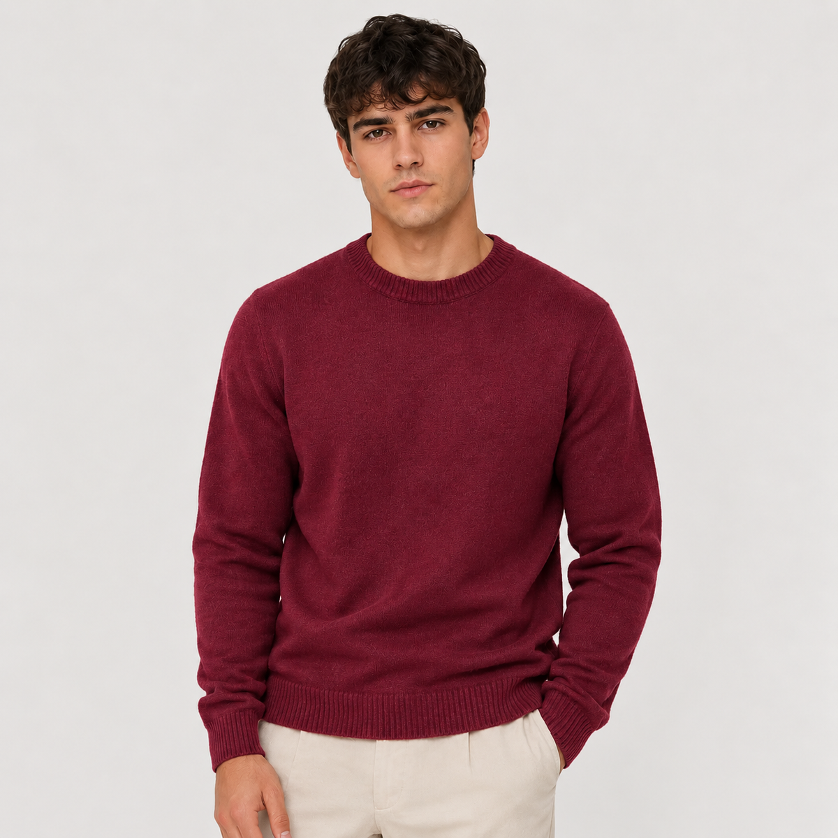 A man wearing a red crewneck knit sweater and matching trousers, standing against a solid light gray background.