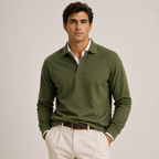 A man wearing an olive green long-sleeve polo shirt over a white collared shirt, paired with cream trousers and a brown belt, standing against a light gray studio background.
