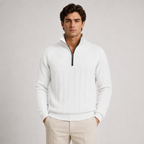 A man wearing a white textured quarter-zip sweater with cable knit details and beige trousers, standing against a light gray studio background.