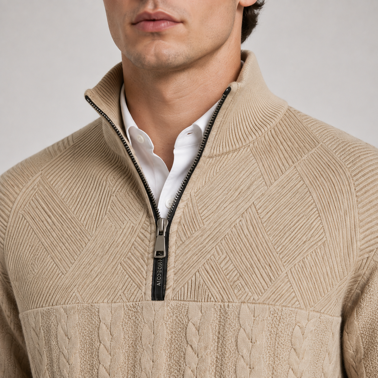 Close-up of a man wearing a beige textured quarter-zip sweater over a white collared shirt, with the zipper pull showing the brand name ARIS.