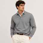 A man wearing a gray long-sleeve polo sweater over a white collared shirt, paired with cream trousers and a brown belt, standing against a light gray studio background.