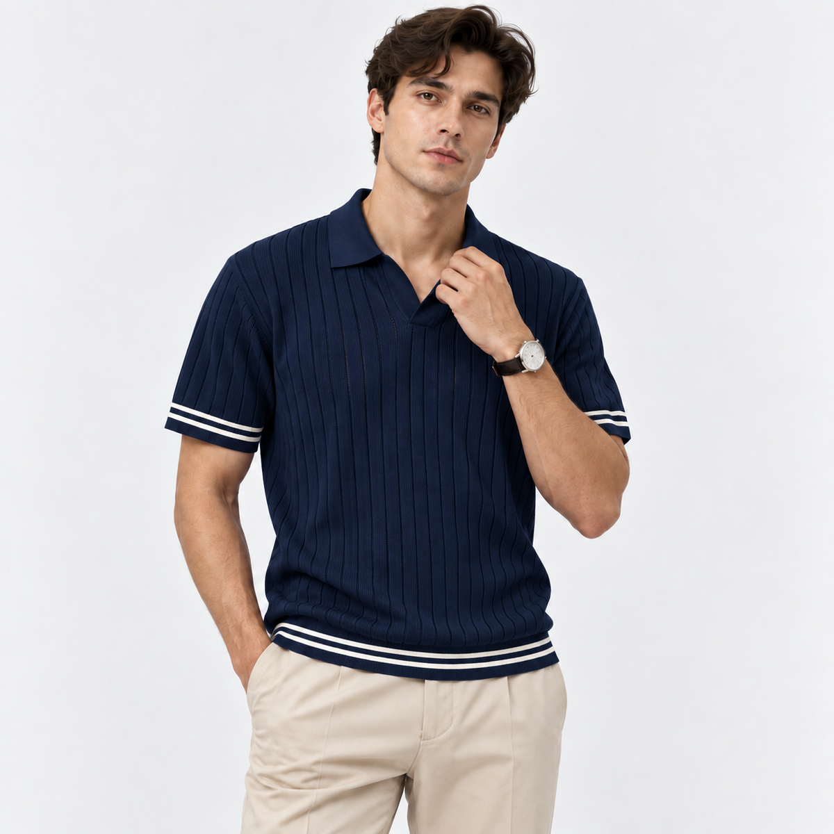 A man wearing a navy blue ribbed short-sleeve polo shirt with white stripes on the sleeves and hem, paired with beige trousers, against a light gray studio background.