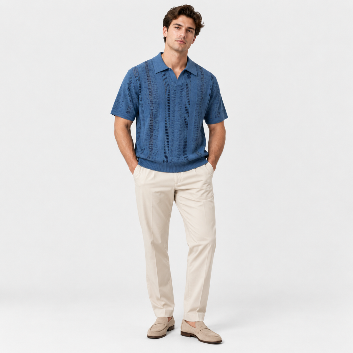 A man modeling a short-sleeve blue button-up shirt with vertical textured stripes, paired with beige trousers and beige loafers, against a light gray studio background.