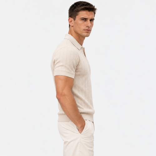 A man in a side profile wearing a light beige short-sleeve knit polo shirt and matching trousers against a plain white studio background.