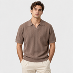 A man wearing a brown short-sleeve knit polo shirt with vertical textured stripes and cream pants, standing against a light gray studio background.