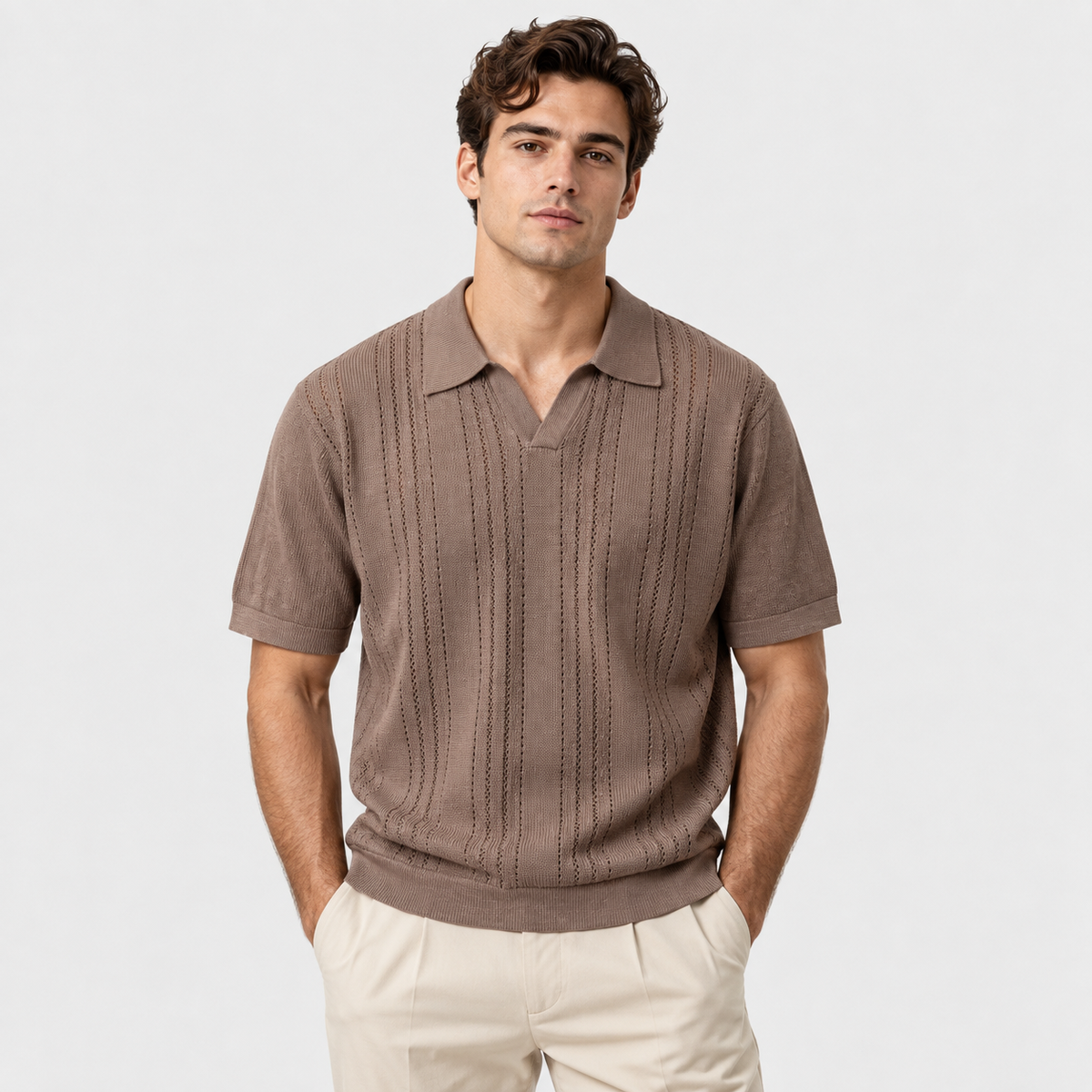 A man wearing a brown short-sleeve knit polo shirt with vertical textured stripes and cream pants, standing against a light gray studio background.