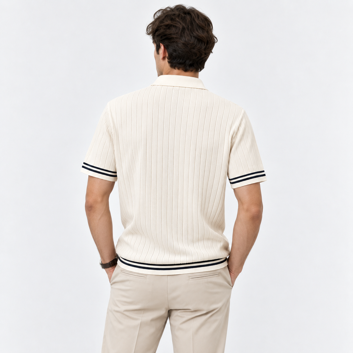 A man viewed from behind wearing a cream ribbed short-sleeve polo shirt with black stripe accents on the sleeve cuffs and hem, paired with beige trousers, against a plain white studio background.