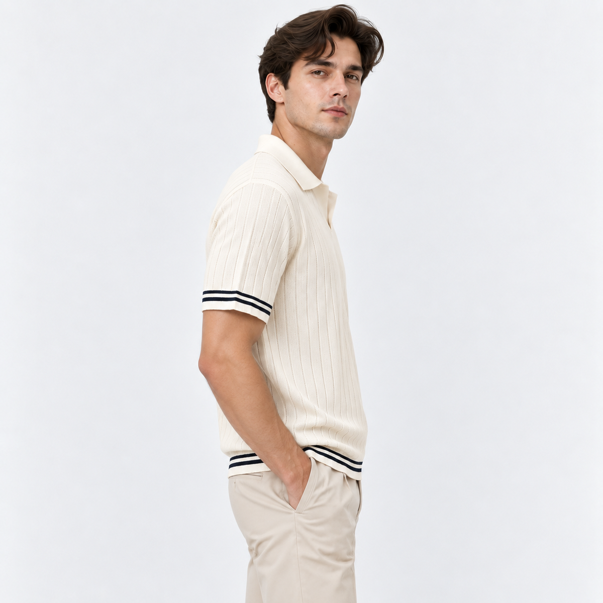 A man wearing a cream ribbed short-sleeve polo shirt with black and white striped cuffs and hem, paired with beige trousers, photographed against a clean white studio background.