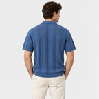 A man viewed from the back wearing a blue short-sleeve knit polo shirt with vertical textured stripes and cream pants, against a light gray studio background.